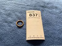 Top view of gold band ring on blue cloth alongside MaxSold lot card