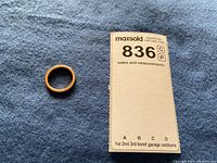 Ring on blue felt next to measurement card marked with lot number.