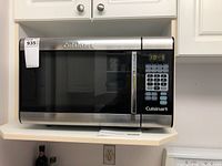 Front view of stainless steel Cuisinart microwave oven on kitchen shelf with digital keypad, brand logo, and control panel showing time.