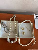 Full lot shown with pearl necklaces, earrings, stick pin, and watch in two separate boxes on a table.