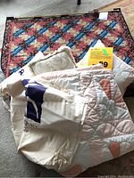 Photo showing folded grandmother's fan patterned quilt and quilted cushions with a visible quilting exhibition bag.