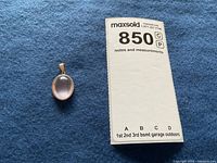Rose quartz pendant placed on blue fabric alongside measurement note for scale.