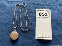 Photo showing the front of the sterling silver engraved locket on the silver-tone chain with size reference card