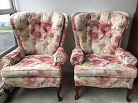 Front view of two floral wing back chairs side by side showing overall condition and pattern.