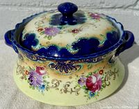 Front and side view of the covered serving dish showing floral design, blue rim, and handles.