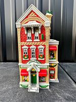 Front view of the cast resin building showing detailed red brick facade with green and white doors and windows, snow accents, and signage for costumes and tuxedos.