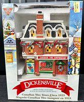 Front view of lighted Canadian Tire store building decoration inside original box, showing brick style, Christmas wreaths, red sign, and yellow illuminated windows.