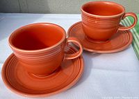Two Persimmon colored Homer Laughlin Fiesta Ware teacups each on matching saucers, shown on white background.
