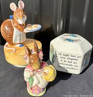 Three items displayed side by side on black background showing Beswick Mrs Rabbit figurine, Schmid squirrel music box, and Wedgwood white hexagonal still bank with Beatrix Potter illustrations.