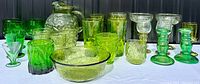 Wide view of entire glassware collection showing various glasses, pitcher, bowls, and candlesticks in shades of green.