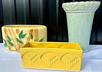 Three vintage ceramic planters shown together: yellow rectangular Art Deco planter in front, bamboo-style planter cream-green behind left, and tall green textured planter behind right