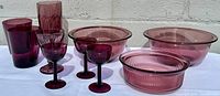 Side view of the amethyst glass bowls and goblets arranged on a white surface in natural light showing color and shapes
