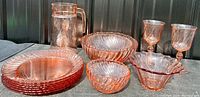 Photo showing entire lot of pink glass dinnerware including plates, pitcher, various bowls, and glasses.