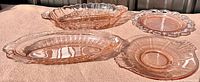 Four pink depression glass dishes displayed in sunlight showing embossed patterns and scalloped edges.