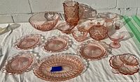 Full view of collection showing various pink depression glass pieces including bowls, plates, pitcher, sugar bowl, and platters on concrete background.
