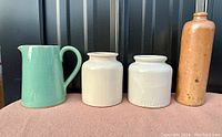 Four vintage stoneware pieces shown on pink cloth with black background: mint green Denby jug, two cream jars including one LAB Lagny marked, and tall tan Bols gin bottle.