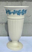 Full view of the Wedgwood Queensware vase showing the overall shape, ribbed cream body, pedestal base and blue relief floral decoration around the rim.