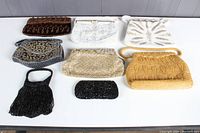 All eight assorted vintage evening bags laid out on a white surface, showing variety in color, size, and bead styles