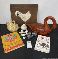 Overall lot showing wooden painted rooster sign, rust-colored duck sculpture, ceramic hen container, smaller bird figurines, and two books.