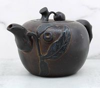 Front side view showing the spout and cherry blossom leaf decoration on the body of the dark brown ceramic tea pot.