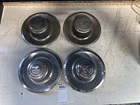 Four original Chevrolet center caps displayed on a table, showing front view and overall condition.