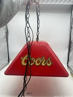Full view of the red Coors branded hanging lamp showing the trapezoidal shape, metal chain, and logo on the side.