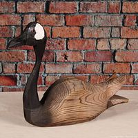 Side view of hand-carved wooden goose decoy showing natural wood grain body and painted head and neck.