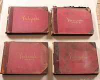 Four red cloth-bound photo albums with leather corners and spines laid flat