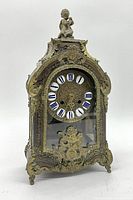 Front view of brass mantel clock showing ornate neoclassical design, porcelain dial with missing number 2 plate, and figural pendulum seen through glass door.
