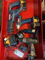 Four Ryobi power tools with 18V battery packs and a battery charger in red container showing condition and quantity