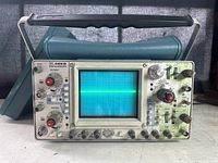 Front view showing the Tektronix 465B oscilloscope powered on with a visible trace on the CRT screen, all controls and labels visible.