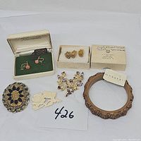 Full view of all jewelry items including the M. Haskell bracelet, Krementz earrings in box, award pins in box, and various brooches.