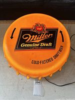 Front view of the vintage Miller Genuine Draft XL beer cap wall light showing detailed logo and branding on a bright orange background resembling a large bottle cap.