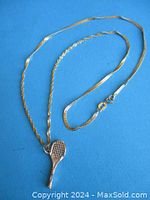 Full view of the 10K gold necklace with tennis racket pendant laid flat on blue background