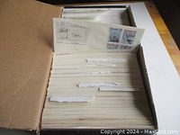 Photo showing a large box filled with neatly organized white envelopes of First Day Covers with visible stamps and postmarks.