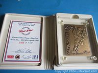 Open white plastic case showing certificate of authenticity and bronze mint-card inside acrylic display case.