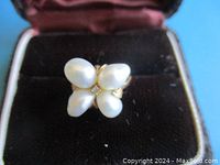 Front view of ring showing four pearls and central diamond in open display case