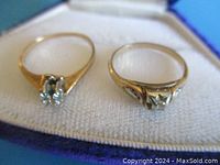 Two rings side by side on white cloth inside jewelry box.
