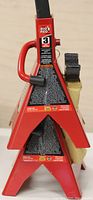 Close-up image of a red Torin Big Red 3 ton jack stand showing the warning label, handle, and attached lock-out safety bar in new condition.