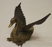 Front view of the vintage brass swan figurine showing detailed feathers, raised wings, and curved neck.