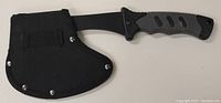 View of the camping axe with blade partially covered by black fabric sheath secured with metal rivets.