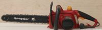 Side view of red and black Homelite electric chainsaw showing 16-inch blade and yellow control knobs.