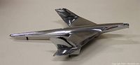 Side view of the polished chrome vintage airplane hood ornament showing its sleek, elongated body and twin vertical stabilizers.