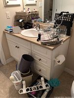Bathroom countertop with various items including rubbish bins, dish rack, towels, flashlight, and cords