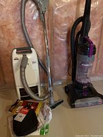 Both vacuum cleaners shown side by side: Bissell PowerForce upright vacuum and Kenmore Whispertone upright canister vacuum with hose and wand and package of vacuum bags.