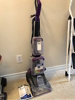 Full front view of the Bissell carpet cleaner with power cord wrapped and user manual on the floor beside it.