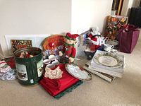 Overall view of Christmas-themed decor, linens, figurines, serving items arranged on floor.