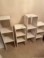 Four white particle board shelving units against beige wall showing height and shelving configuration.