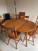 Overall view of round wooden dining table with six chairs, showing table top with one leaf and arrangement of chairs.