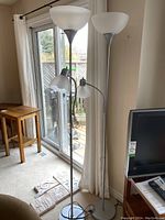 Pair of floor lamps placed indoors near sliding glass door and curtains. Lamps have large frosted glass bowl on top and smaller adjustable reading lamp with frosted glass shade on the pole.